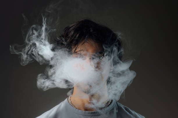 A person exhales dense, swirling white vape smoke that partially obscures their face.