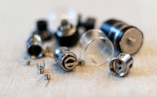 Various disassembled vape atomizer parts, including metal components, a clear tank, and small coils, laid out on a light-colored fabric surface, relevant to topics about vape maintenance and atomizer structure.